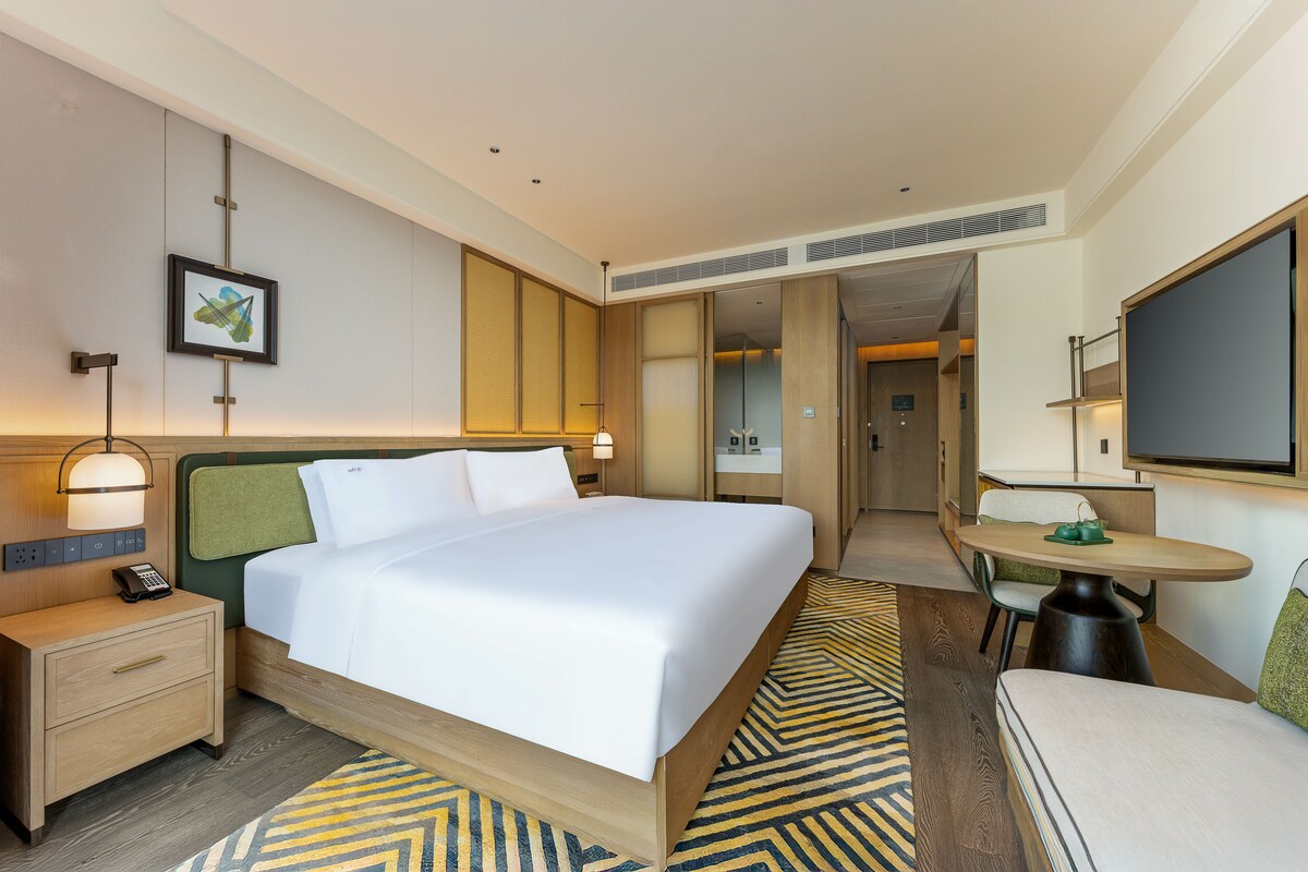 Una habitación de hotel con una cama grande, mesitas de noche, un escritorio y un televisor.