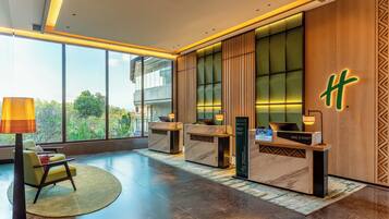 A hotel reception area with a modern design, featuring a reception desk, seating area, and large windows offering a view of the outdoors.
