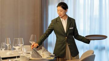 Una persona con un blazer verde y camisa blanca atendiendo una mesa con copas de vino, platos y cubiertos.