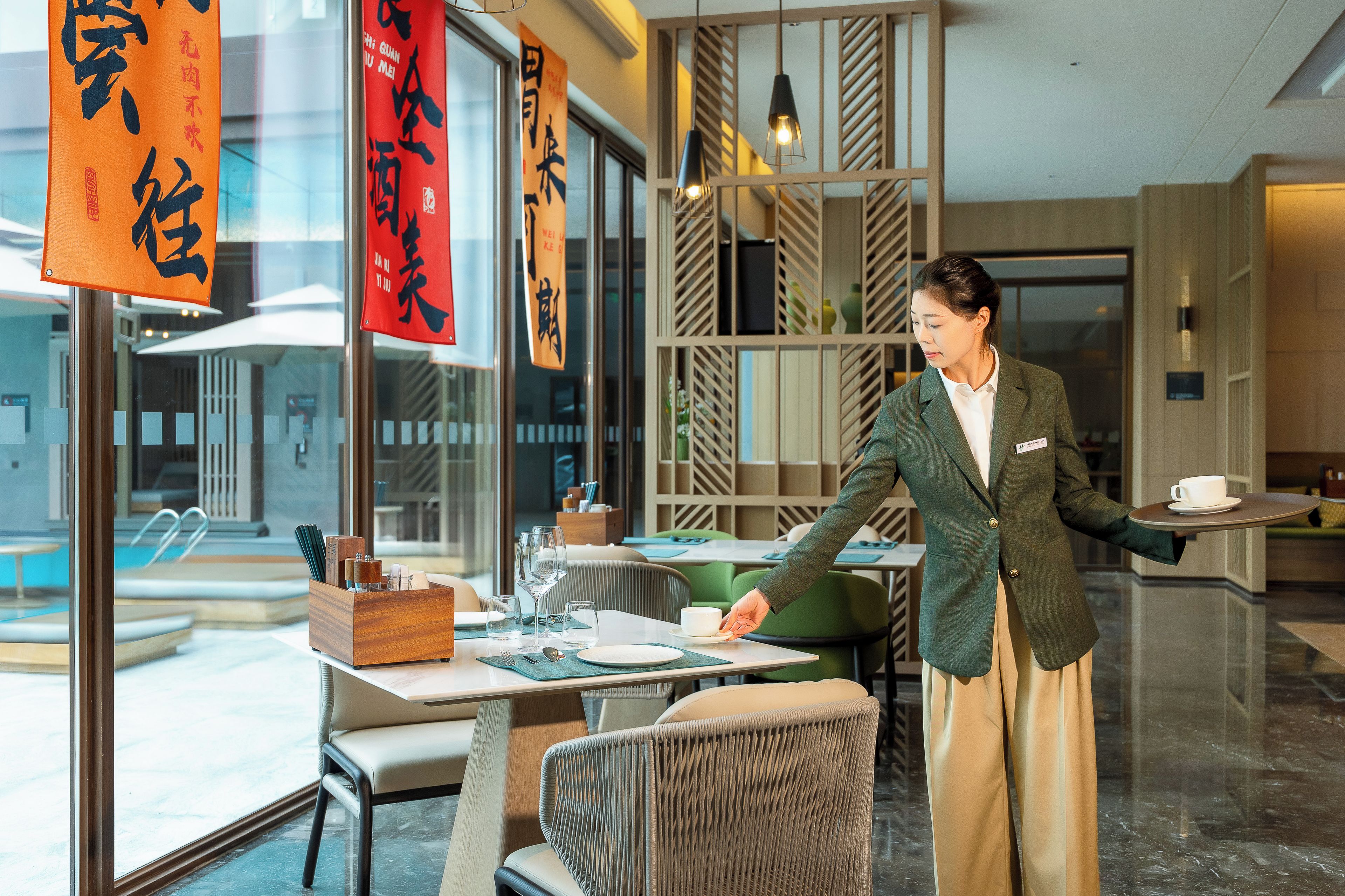 A hotel interior with a dining area, a reception desk, and a view of the outside.