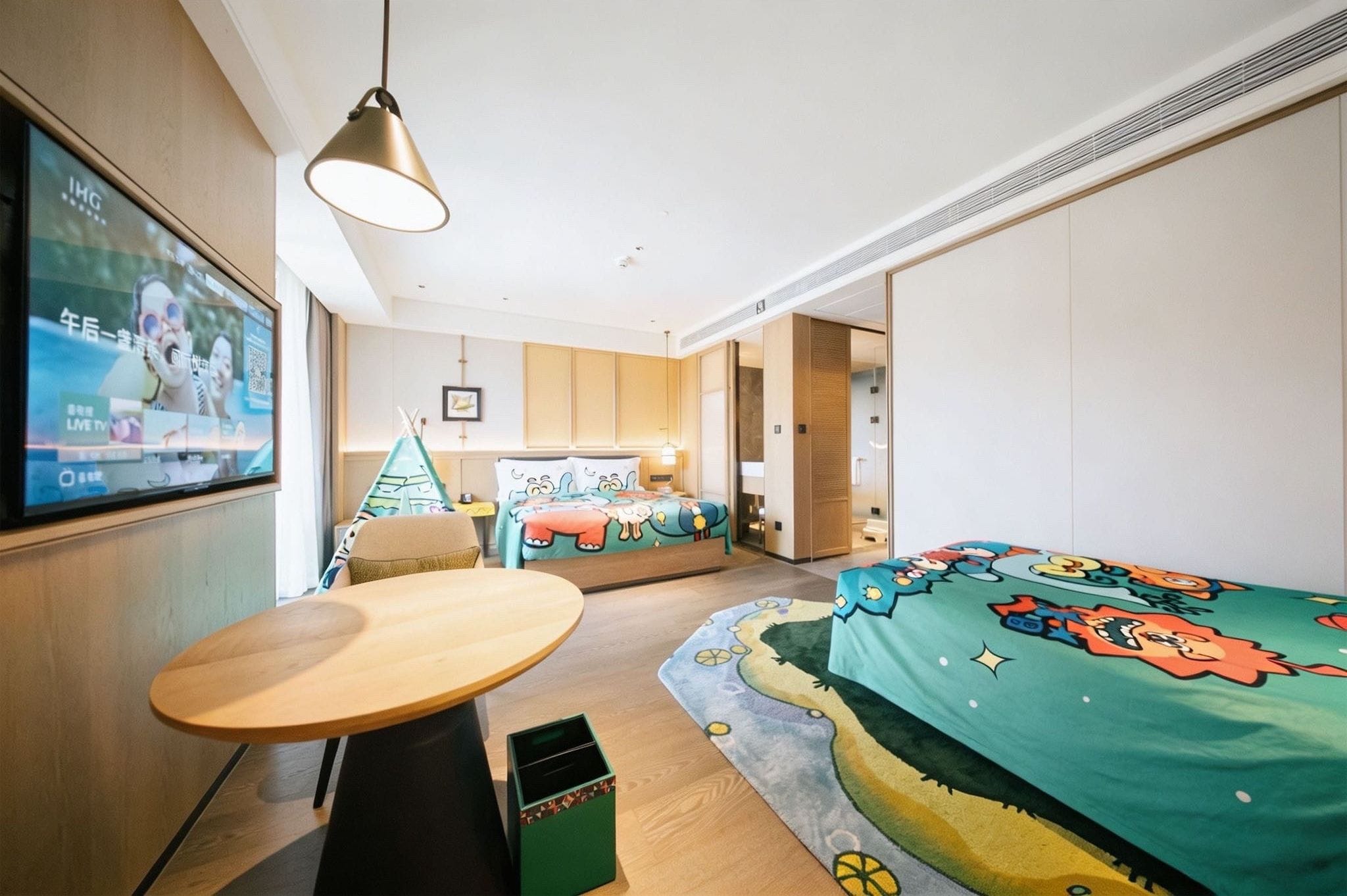 A hotel room with a bed, a small table, a TV, and a wall-mounted shelf.