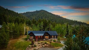 Une cabane en rondins à deux étages, surmontée d’un toit en métal, entourée d’un paysage boisé et avec une montagne en arrière-plan.