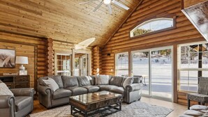 L'intérieur d'une cabane en rondins, avec un canapé d'angle, une table basse et une vue sur un paysage enneigé par de grandes fenêtres.