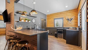 Une cuisine moderne dotée d’un îlot central, de tabourets de bar, de luminaires suspendus et d’un mur d’accent en bois.