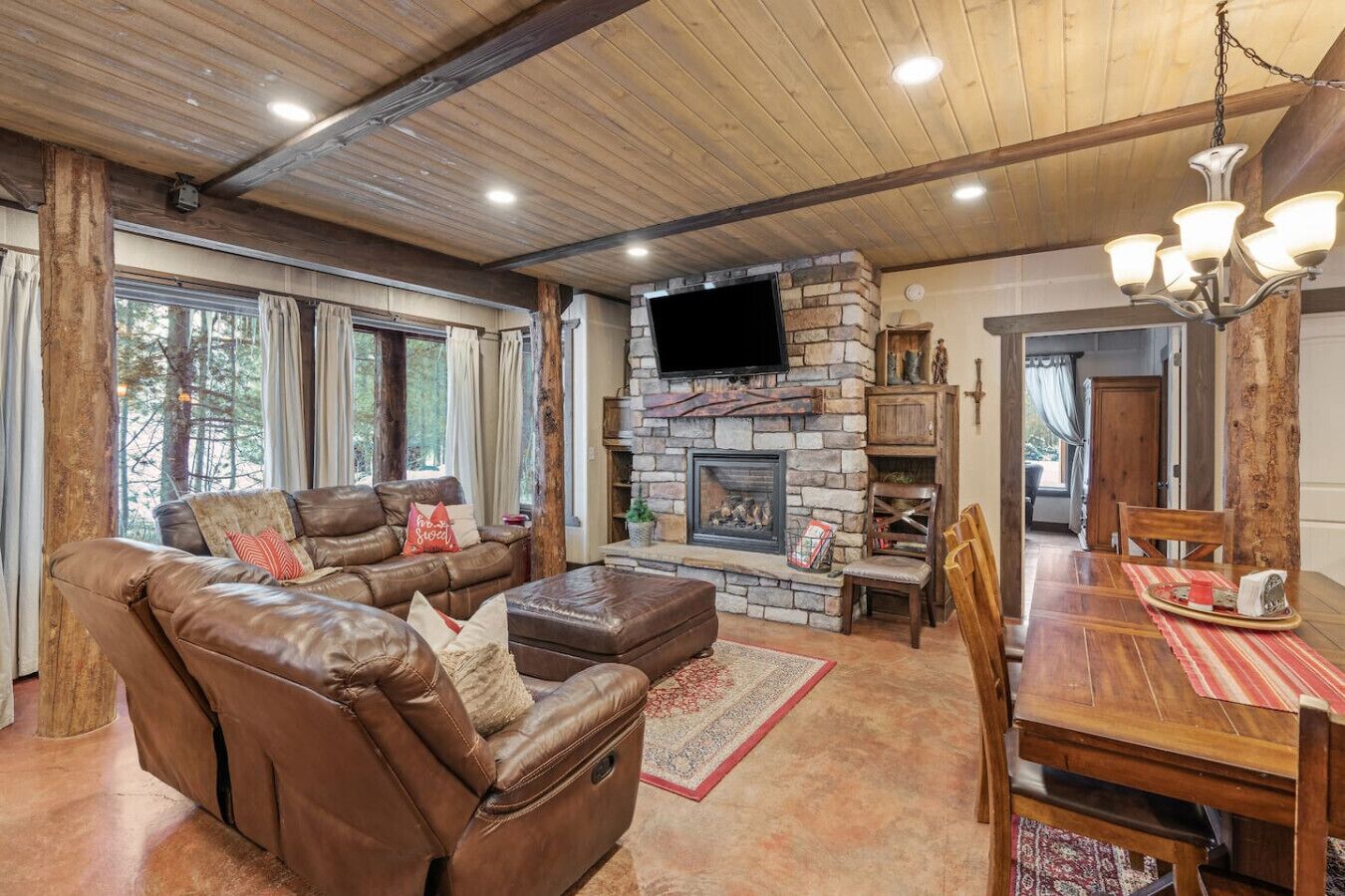 A cozy living room with a stone fireplace, leather sofa, and a dining area with a wooden table and chairs.