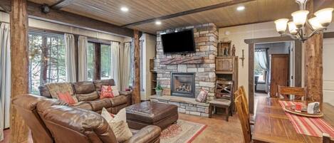 A cozy living room with a stone fireplace, leather sofa, and a dining area with a wooden table and chairs.