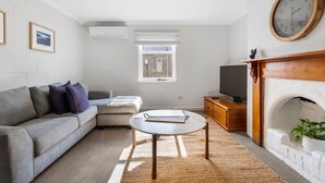 Una sala de estar moderna con un sofá gris, una mesita redonda pequeña, un televisor y una chimenea.