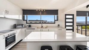 A modern kitchen with a large island, white cabinetry, and a view of the landscape through large windows. - Expansive River-View Oasis (Claremont)