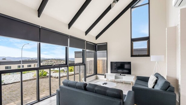 A modern living room with large windows, a flat-screen TV, and two grey sofas. - Expansive River-View Oasis (Claremont)