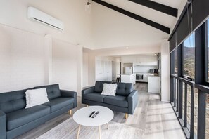A modern living room with two sofas and a coffee table, a kitchen in the background, and large windows. - Expansive River-View Oasis (Claremont)