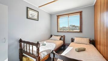 A bedroom with two wooden beds, a window with blinds, a framed picture on the wall, and a wooden headboard.