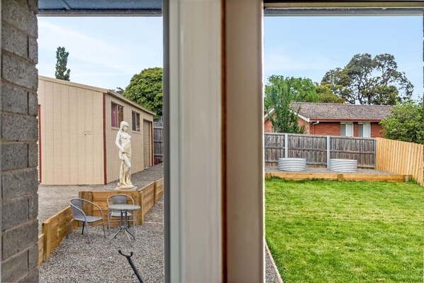 A view through a window of a backyard with a wooden deck, a statue, and a fenced area.