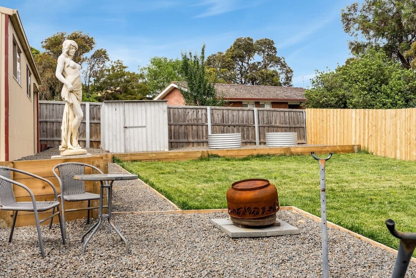 A backyard with a statue, a barbecue grill, and a wooden deck.