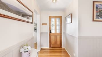 A hallway with a wooden door, framed artwork on the walls, and a vase with flowers on a white bench.