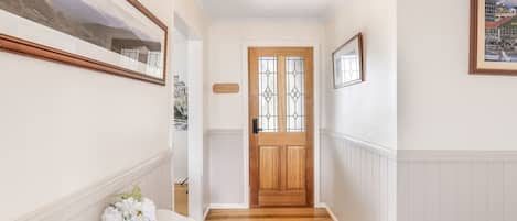 A hallway with a wooden door, framed artwork on the walls, and a vase with flowers on a white bench.