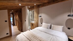 A bedroom with a wooden ceiling, a large bed with white bedding, a wooden nightstand, and a wooden wardrobe. - 7 minutes from the center and superb mountain views (Megève)