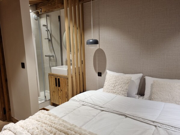 Un dormitorio con una cama grande, un armario de madera, una cabina de ducha de vidrio y una lámpara colgante.