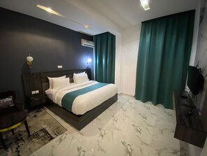 Habitación de hotel con cama, escritorio, silla, televisor y ventana con cortinas.