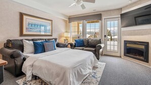 Ein Schlafzimmer mit einem Bett, zwei Ledersofas, einem Kamin, einem Deckenventilator und einem großen Fenster.