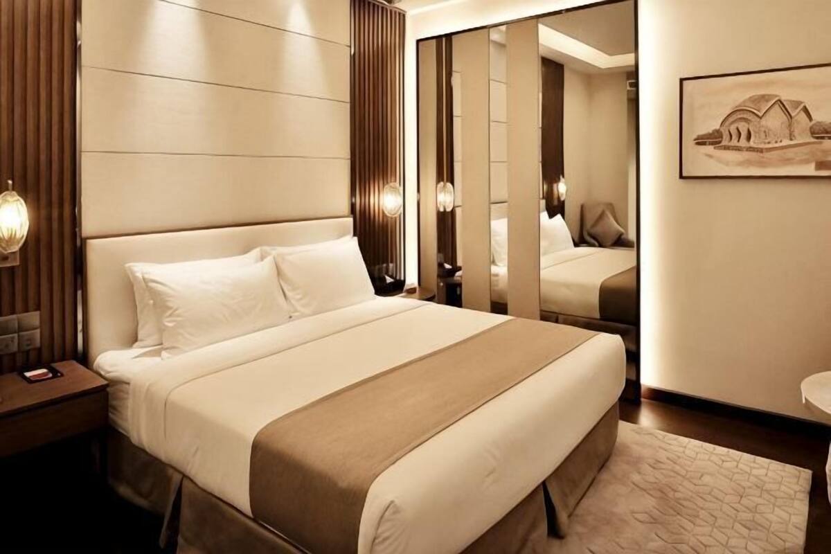 Une chambre d’hôtel avec un grand lit, une table de chevet, un miroir et un tableau encadré au mur.