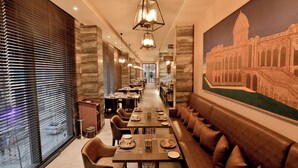 A long dining area with tables set for meals, a large mural of a historical building, and a view through large windows.
