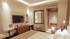 A hotel room with a large bed, a desk with a mirror, a small round table, and a separate seating area with a chair.
