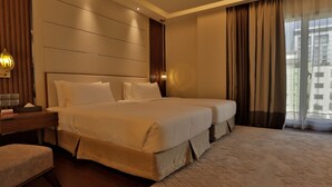 A hotel room with a large bed, a desk, a chair, and a window with curtains.