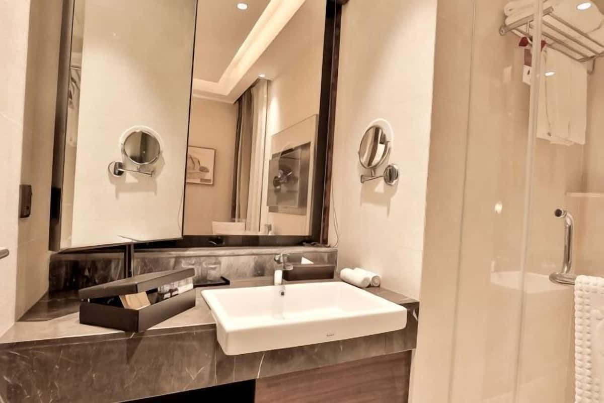 A modern bathroom with a large mirror, a white sink, and a glass shower enclosure.