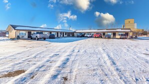 Un bâtiment avec un parking recouvert de neige, plusieurs véhicules stationnés et un ciel bleu dégagé parsemé de nuages.