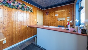 Une salle d’attente avec des panneaux de bois, un comptoir recouvert de papiers, une petite plante et une fenêtre avec des stores.