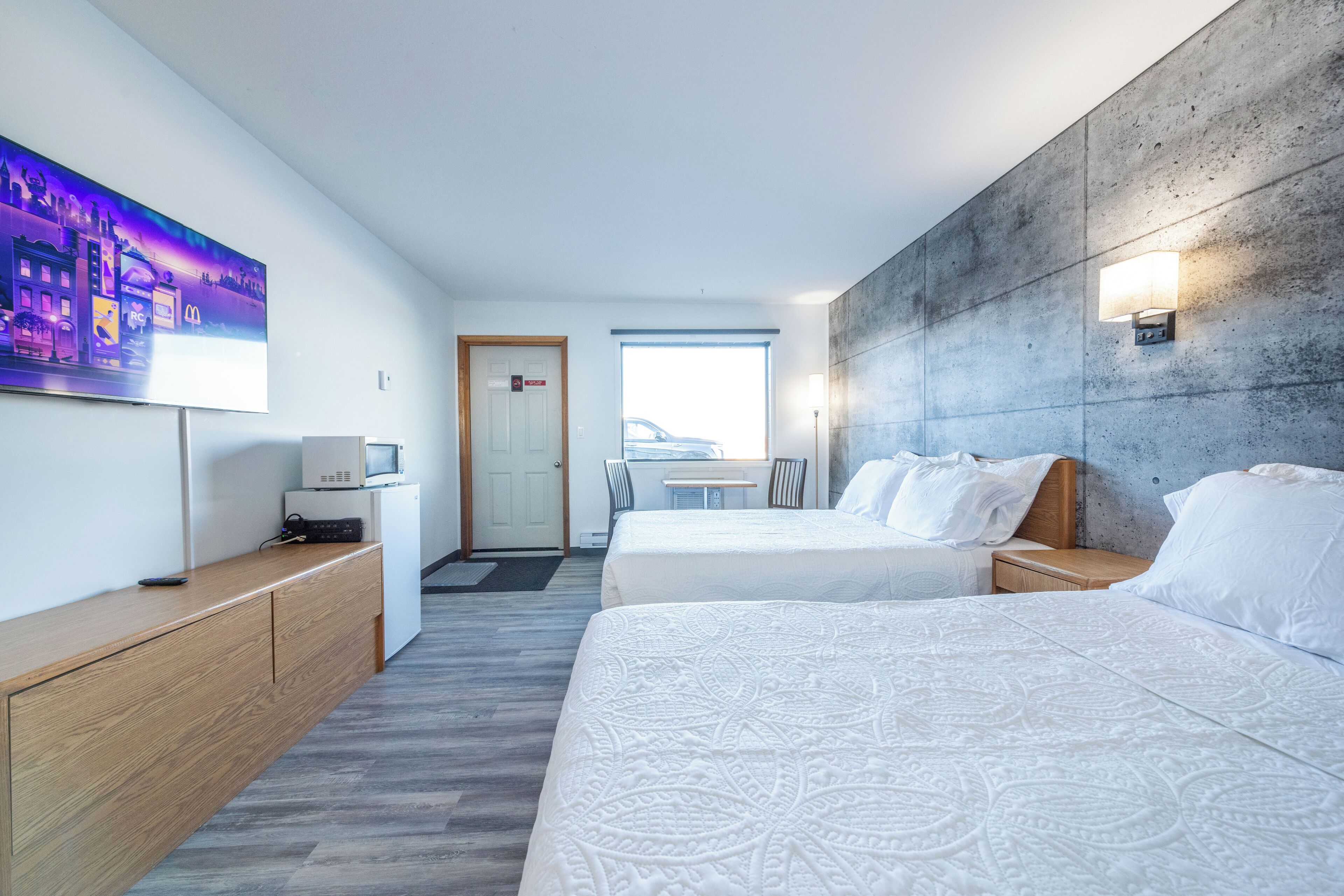 A hotel room with two beds, a desk with a computer, a flat-screen TV, and a large window.