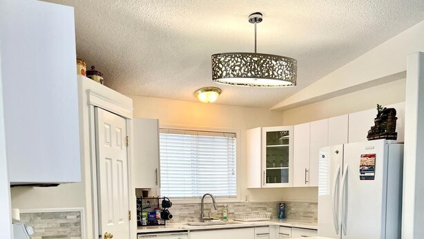 A modern kitchen with white cabinetry, a central island with bar stools, and a pendant light. - Fort McMurray Home - 4 Bedroom House: Perfect for Families & Business (Fort McMurray)