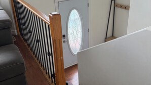 A staircase with a wooden handrail, a grey cushioned bench, and a white door with a stained glass window. - Fort McMurray Home - 4 Bedroom House: Perfect for Families & Business (Fort McMurray)