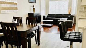 A modern living room with a dining area, featuring a sofa, chairs, a coffee table, and a bar stool. - Fort McMurray Home - 4 Bedroom House: Perfect for Families & Business (Fort McMurray)