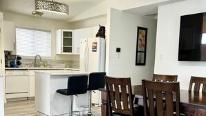 A modern kitchen with white cabinetry, a central island, and a dining area with wooden chairs and a table. - Fort McMurray Home - 4 Bedroom House: Perfect for Families & Business (Fort McMurray)