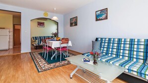 Ein Wohnzimmer mit einer Couch, einem Esstisch mit Stühlen, einem kleinen Tisch mit einer Vase und einem Gemälde an der Wand.