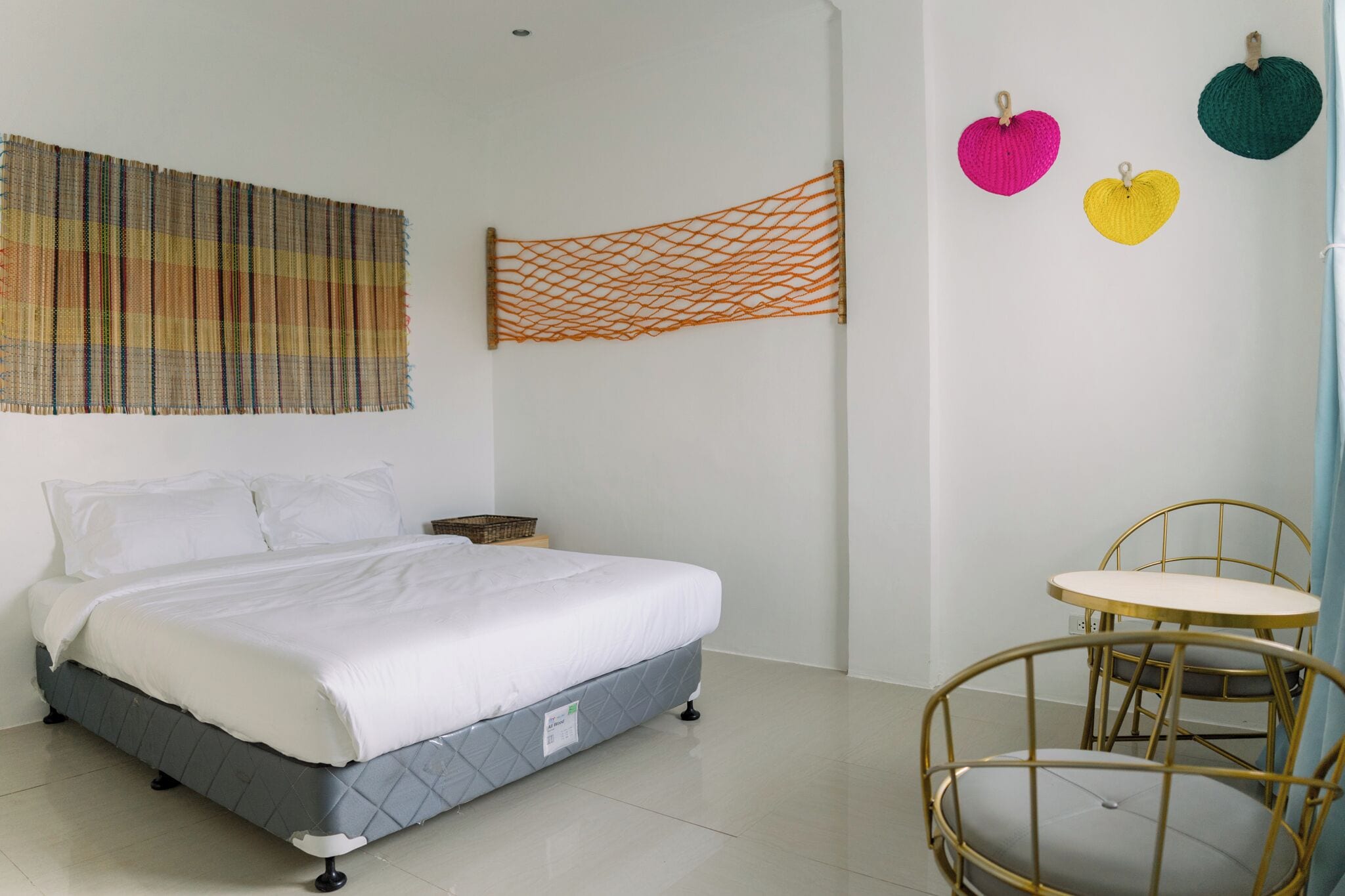 A bedroom with a bed, a small table with chairs, and a wall hanging.