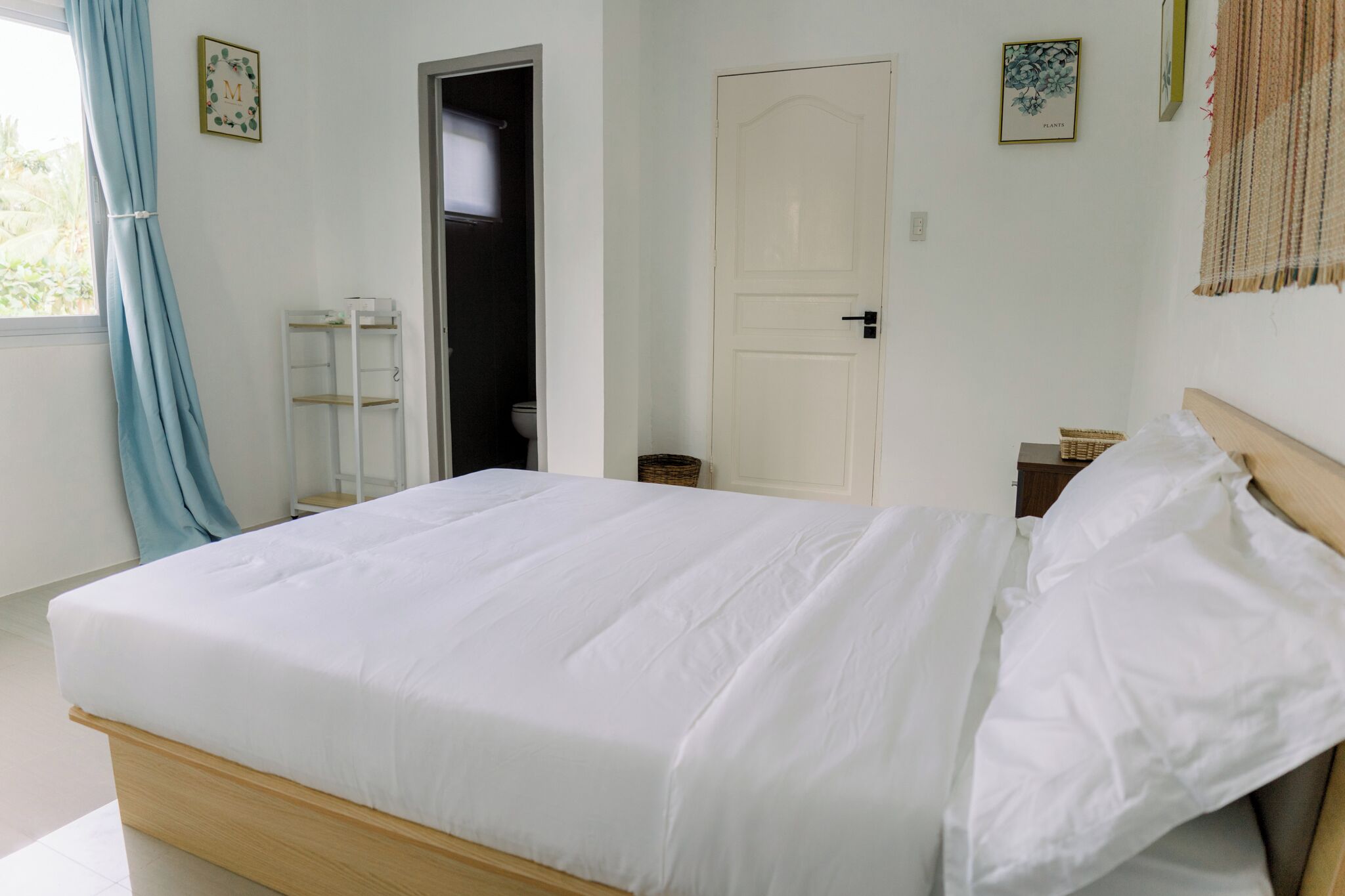 A neatly made bed with white linens, a wooden headboard, and a white door with a small window.