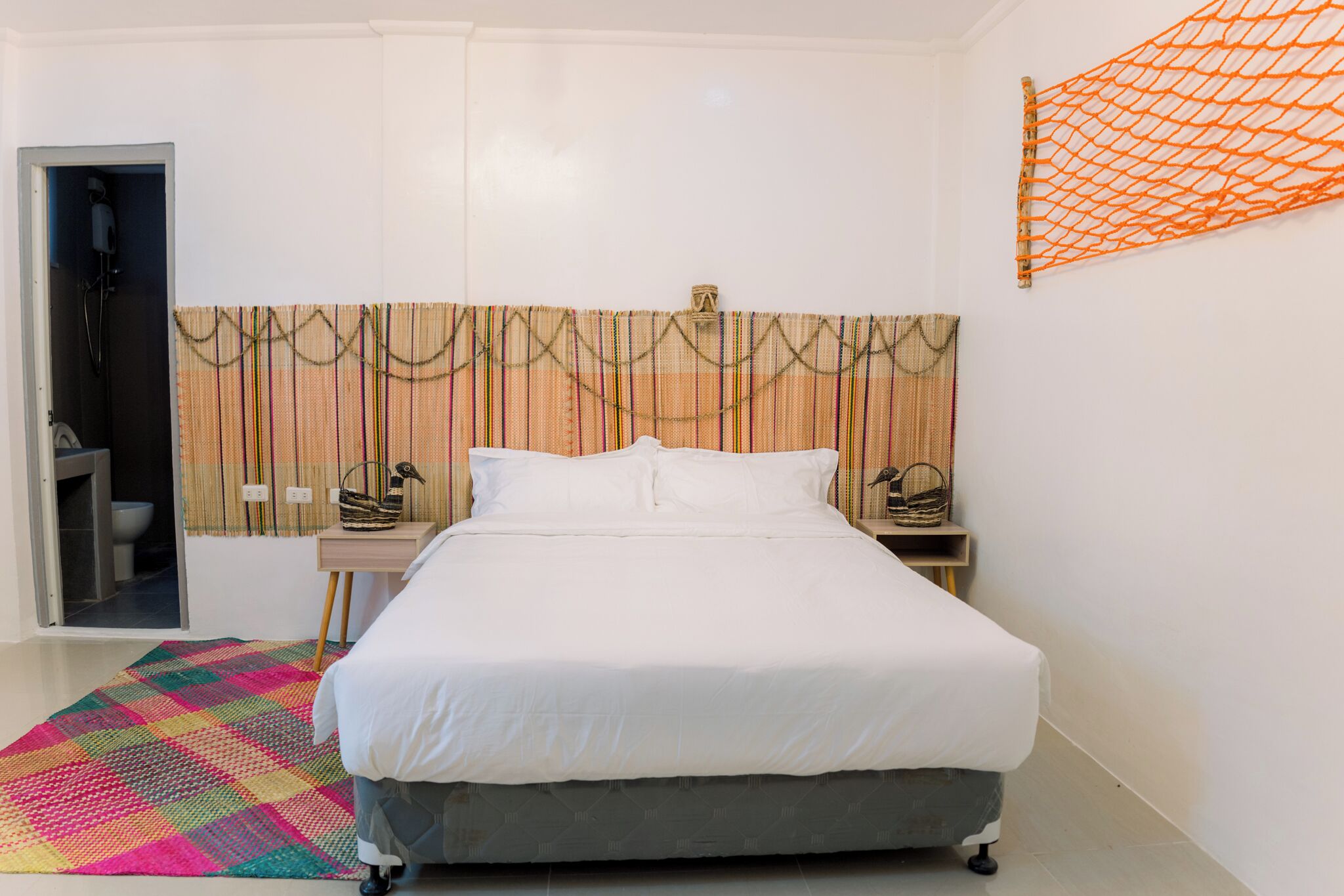 A neatly made bed with white linens, a colorful checkered rug, and a headboard with a striped pattern.
