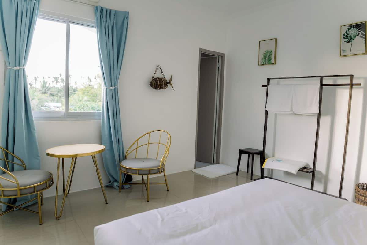 Habitació d'hotel amb un llit, dues cadires, una taula petita, un penjador de tovalloles i una porta que condueix a una altra habitació.