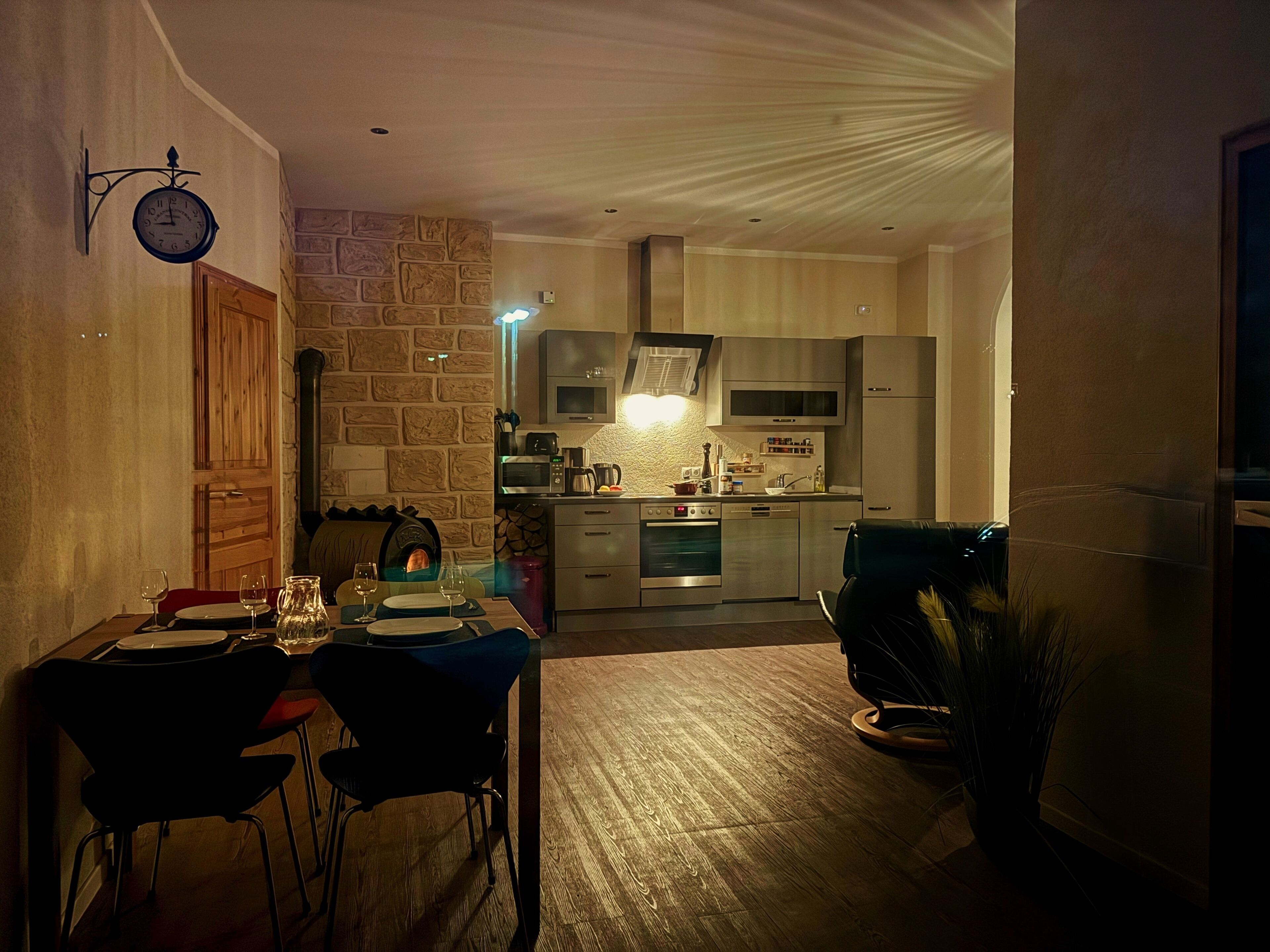 Een gezellig eetgedeelte met een stenen muur, een klok en een moderne keuken op de achtergrond.