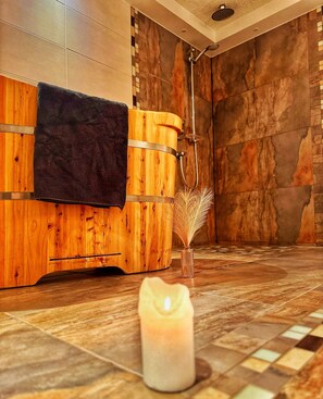 Puinen sauna, jossa on pyyhe, suihkupää ja kynttilä lattialla.