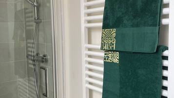 Une salle de bain dotée d’une douche à parois de verre, d’un porte-serviettes blanc sur lequel est posée une serviette verte, et d’un panneau de commande de la douche bien visible.