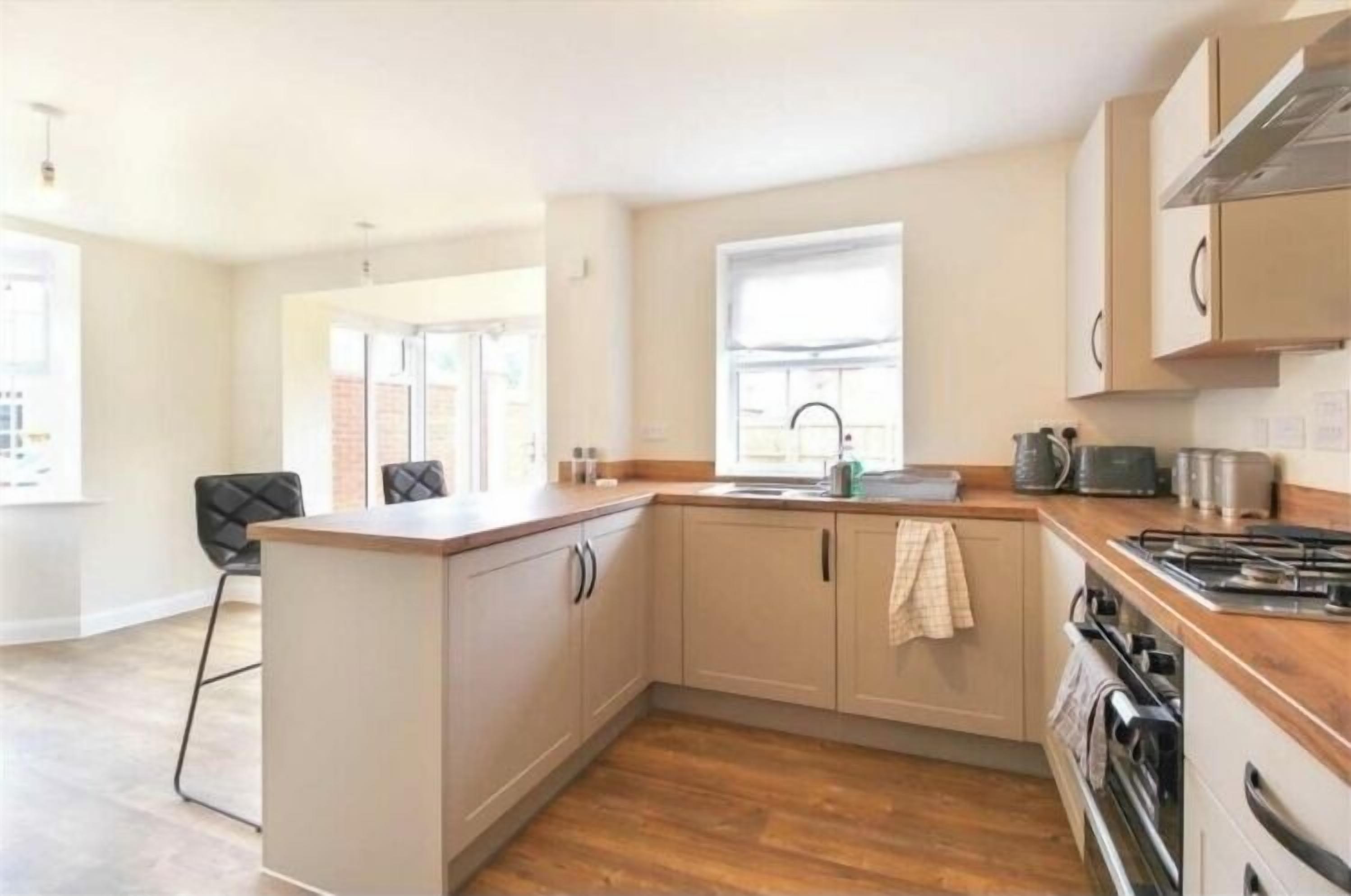 A modern kitchen with light-colored cabinets, a wooden countertop, a gas stove, and a window providing natural light.