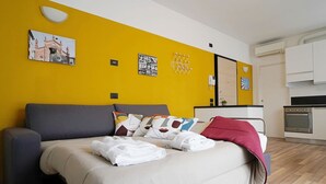 A modern hotel room with a bright yellow accent wall, a bed with a grey headboard, and a small kitchenette in the background. - Studio With Balcony in Bovisa Milan (Milan)
