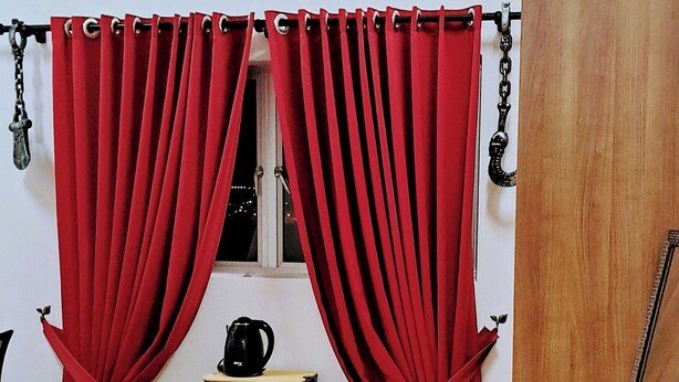 A bedroom with a bed, red curtains, a ceiling fan, a clock, a small table with a kettle, and a wooden cabinet. - The Red Room @ Alanis Residence Sepang, KLIA1 and KLIA2 (Sepang)