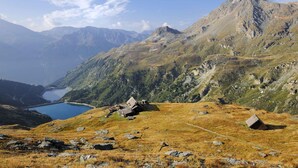 Un paysage montagneux avec un lac aux eaux limpides, un terrain rocheux et une petite cabane.