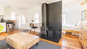 A modern kitchen with a stove, oven, and a black wood-burning stove. There is a dining area with a wooden table and a chair. - Charming Ballard Cottage Retreat with Cozy Fireplace (Seattle)