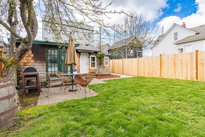 A backyard with a wooden deck, a barbecue grill, and a dining area with chairs and a table.