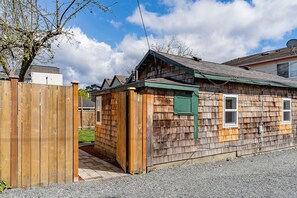 A wooden cabin with a small attached shed, a gravel driveway, and a wooden fence.